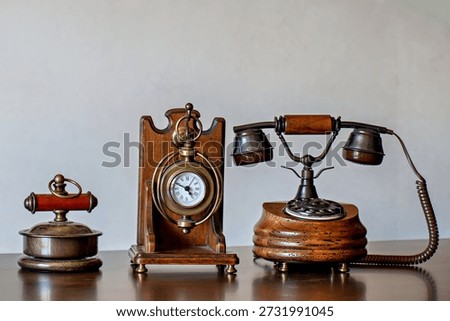 Three antique items on a table: a clock a lamp and a telephone..