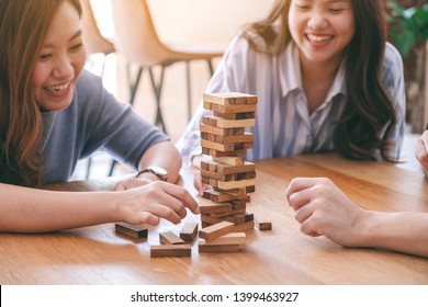 Three Asian Friends Sitting And Playing Tumble Tower Wooden Block Game Together With Feeling Happy