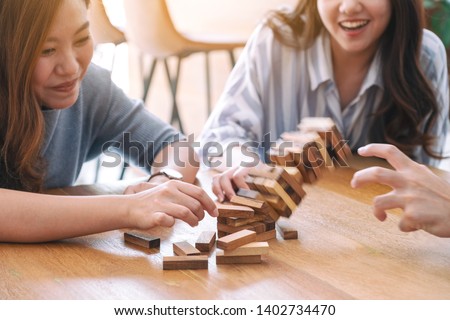 Three asian friends sitting and playing Tumble tower wooden block game together with feeling happy