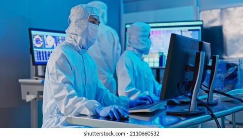 Three Asian Technicians In Sterile Coverall Are Working With Computer At Semiconductor Manufacturing Plant