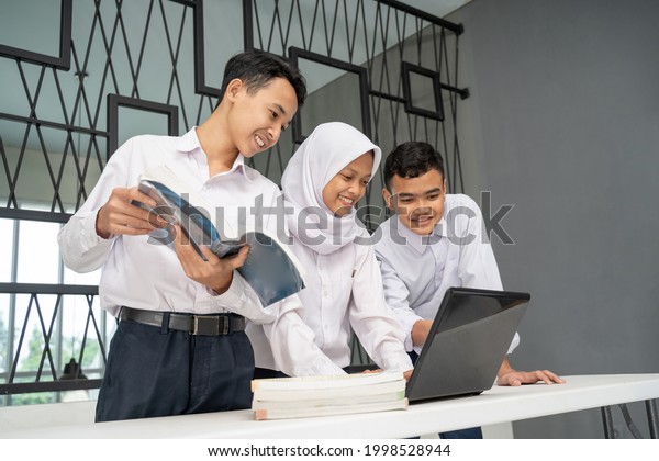 three Asian\
teenagers study together in school uniforms using a laptop and\
several books on the table in the\
room