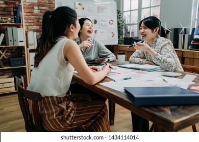 Three Asian Woman Coworkers Laughing At Funny Joke While Meeting In Office. Girls Colleagues In Friendly Work Team Enjoying Positive Emotions And Discussing Project Together. Group Of Happy Partners