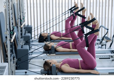 Three Asian women in pink sportswear doing pilates exercises with a reformer bed.  - Powered by Shutterstock