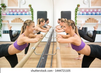 Three athletes exercising hip extension with ball using barre in front of mirror at gym