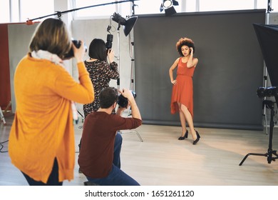 Three attendees  standing in studio and taking photos of beautiful mixed race female model.