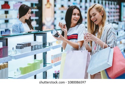 Three attractive young girls are doing shopping with shopping bags in perfume store in modern mall.