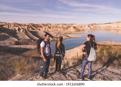 three backpacker excursionists friends smiling and standing in front of a like on top of a desert-like scenario