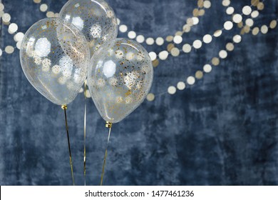 Three Balloons With Confetti And Gold Garlands On A Smoky Dark Blue Background. Birthday And Holiday Decor.