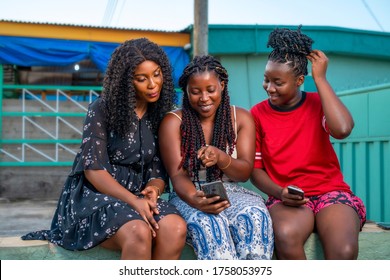 Three Beautiful Black Women In Braids Cheerfully Looking At Phone,having A Voice Call Conversation Excitedly,making Video Call,sharing Data On Social Media Platform,using Mobile Tracking App 