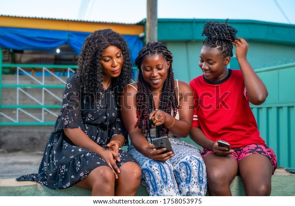 Three\
beautiful black women in braids cheerfully looking at phone,having\
a voice call conversation excitedly,making video call,sharing data\
on social media platform,using mobile tracking app\
