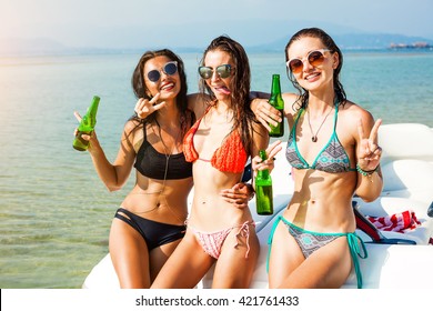 Three beautiful cheerful wet hipster girl at the beach on a tropical island, sitting on the speedboat, drink beer, merry company, sexy bikinis, sunglasses, crazy emotions, grimace, sea