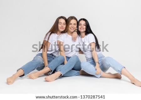 Three beautiful and funny young women in white t-shirts and jeans on a white background.