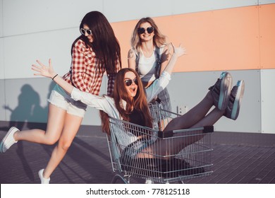 three beautiful girls in sunglasses have fun in the grocery cart under the supermarket in the summer
