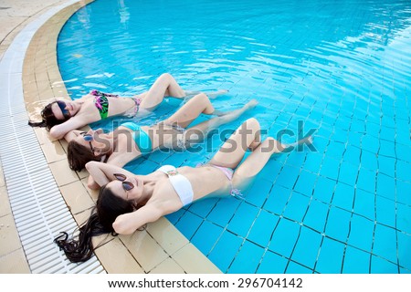 Three beautiful girls in swimsuits lying in a pool of water on vacation