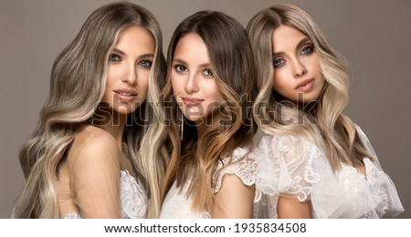 Three beautiful girls in  white wedding dresses  with hair coloring in ultra blond. Stylish hairstyle curls done in a beauty salon. Fashion, cosmetics and makeup.Adorable brides ストックフォト © 