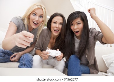 Three Beautiful Interracial Young Women Friends At Home Having Fun Playing Computer Games Together And Laughing