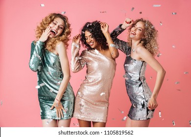 Three Beautiful Laughing Women In Shiny Dresses Dancing Under Confetti Rain Isolated Over Pink Background