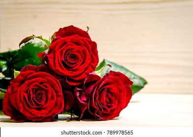 Three beautiful red roses lie on a wooden surface.
