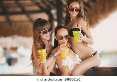 Three Beautiful Sexy Women In Bikini In Bar On Hawaii At Beach Bar. Beautiful Girls Enjoying Alcoholic Beverage Cocktail Outside. Smiling Happy Caucasian Women On Hawaiian Beach.