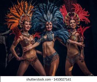 Three beautiful smiling womans in traditional brasilian carnaval costumes are posing for photographer at studio.