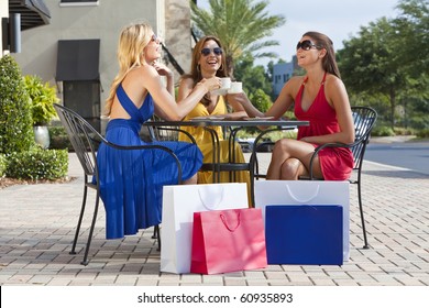 Three Beautiful And Sophisticated Young Women Friends Wearing Sunglasses And Having Coffee Around A Modern City Cafe Table Surrounded By Shopping Bags