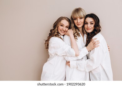 three beautiful women of European appearance hug and smile on a pink background. Several ladies in white shirts. Female friendship.