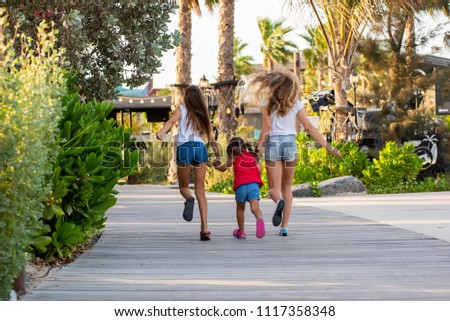 Three beautiful young girls running along the street on La Mer Beach in Dubai