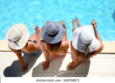 three beautiful young woman with sun hat sitting by the poolside of a resort swimming pool during summer holiday - Powered by Shutterstock