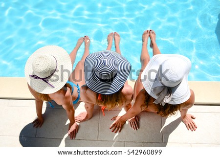 three beautiful young woman with sun hat sitting by the poolside of a resort swimming pool during summer holiday