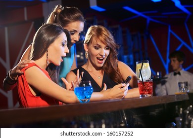 Three beautiful young women friends having fun looking at something funny on their smart phone and laughing