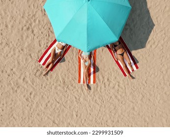 Three beautiful young women lying on the beach sunbathing in swimming suites, relaxing and enjoying. - Powered by Shutterstock