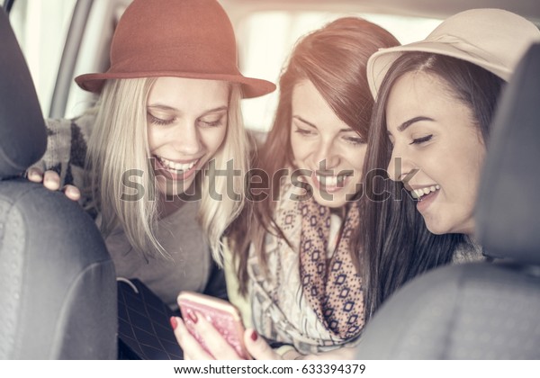 Three best friends in the car and\
riding ridiculous message. Girl showing her friends\
messages.
