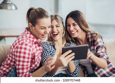 Three best friends using digital tablet together. Women sitting on sofa having fun surfing on the internet using smart digital pc tablet modern device - Powered by Shutterstock