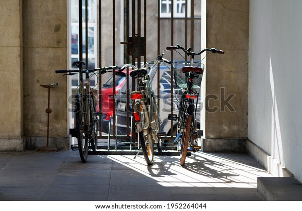 Three bicycles parked at the\
gate. Shaded gate with shade and sun. Bicycles visible from the\
rear. Parked cars in the background.                              \

