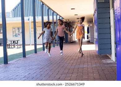 Three biracial girls are holding hands and walking through a school corridor with copy space. They appear joyful, with the school lockers and notice boards creating an educational backdrop. - Powered by Shutterstock