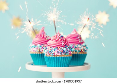 Three birthday cupcakes with pink frosting and party sparklers
