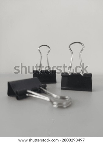 Three black binder clips of different sizes arranged on a plain white surface. Close-up view highlighting essential office stationery, school supplies, business document organization, and paperwork tools.