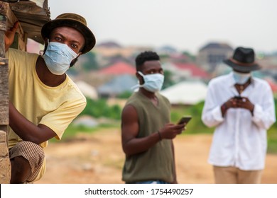 Three black men wearing surgical face masks with two out of focus pressing their phones,sharing data on social media, practicing social distance-A young man wearing a mask looking at camera