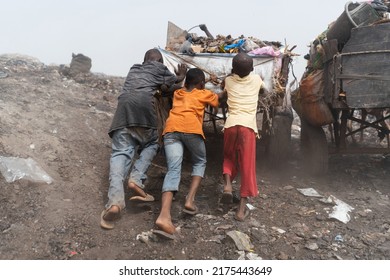 Three Black Street Boys Pushing A Heavy Garbage Cart Up A Heap In Urban Landfill; Informal Waste Management In Africa