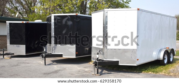 Three black and white transport trailers for sale or\
rent in a row.