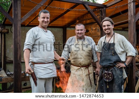 three blacksmiths stand in the background of the workshop. demonstration of ancient technologies at the festival of medieval culture