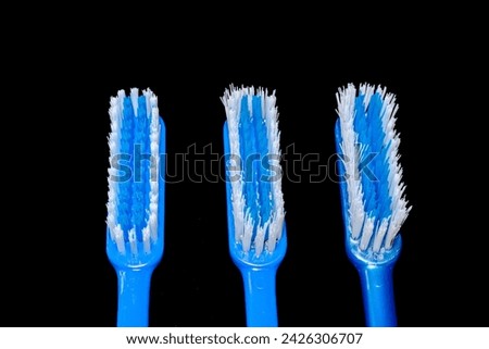 Three blue colored toothbrushes heads isolated in black background. One new with clustered bristles, one used for three months and one used longer with disheveled, bristly and shaggy feather.