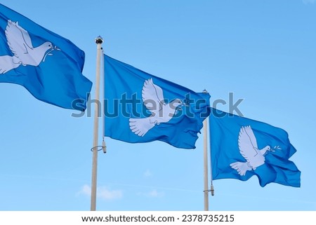 Three blue peace flags in a row printed with a dove with an olive branch in its beak. The dove with the branche is the international symbol of peace.