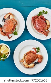 
Three boiled stone crabs on white plates with lemon and parsley on a blue surface. Top view 

