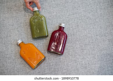 Three bottle of cold pressed juice. Hand holding a glass bottle of orange, berry and vegetable cold pressed drink for take away.