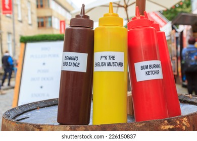 Three Bottles For BBQ Sauce, Mustard, And Ketchup With Funny Labels On A Market