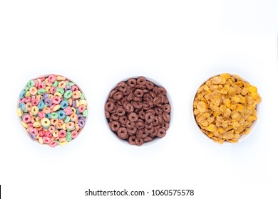 Three bowls of cereals on white background. A bowl of colored cereals, another of chocolate rings and another with corn flex. Top view. Isolated.