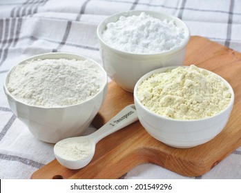 Three bowls with gluten free flour - rice flour, millet flour and potato starch and spoon with xanthan gum