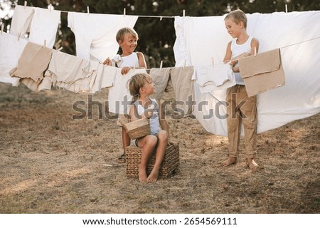 Three boys having fun while hanging laundry on a backyard clothesline, clipping clothes with wooden clothespins. Laughing, playful teamwork and childhood responsibility in natural light
