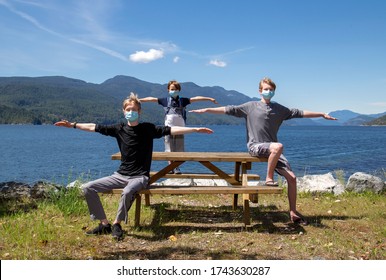 Three Boys At A Picnic Table In A Park Showing Physical Distancing And Wearing Face Masks.